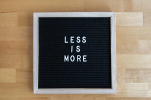 A black letter board with white letters spelling 'Less is More' on a wooden table.