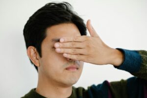 Close-up portrait of a man covering his eyes with his hand in a neutral background.