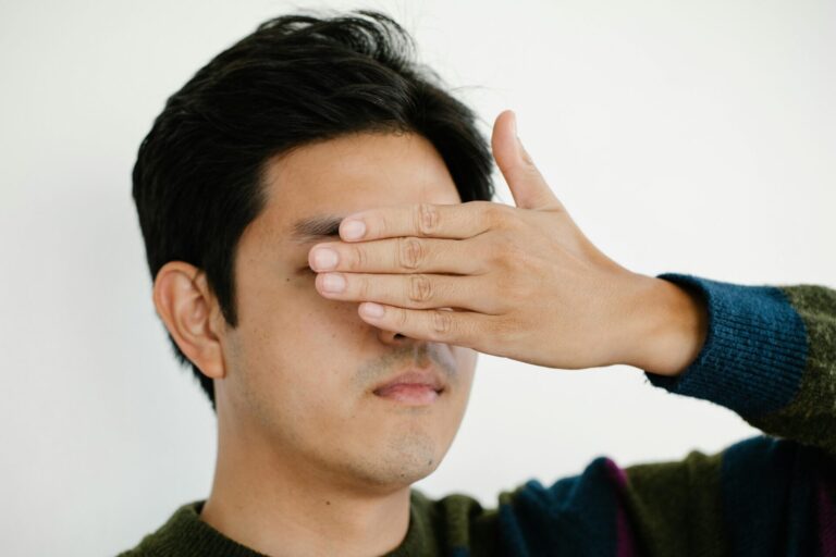 Close-up portrait of a man covering his eyes with his hand in a neutral background.