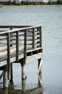 A rustic wooden pier extends over a tranquil lake, surrounded by serene waters under a clear sky.